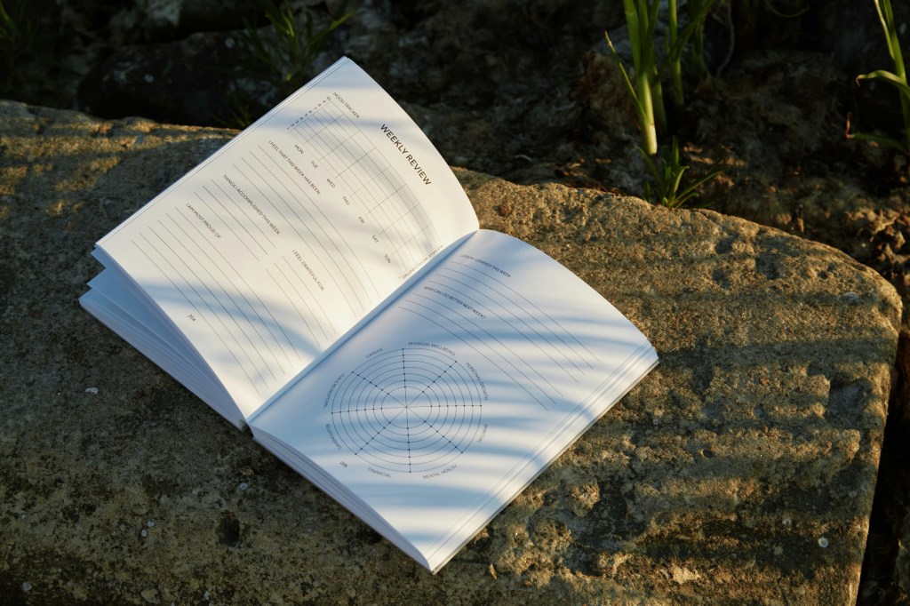 Carnet ouvert posé sur un rocher, éclairé par la lumière du soleil.